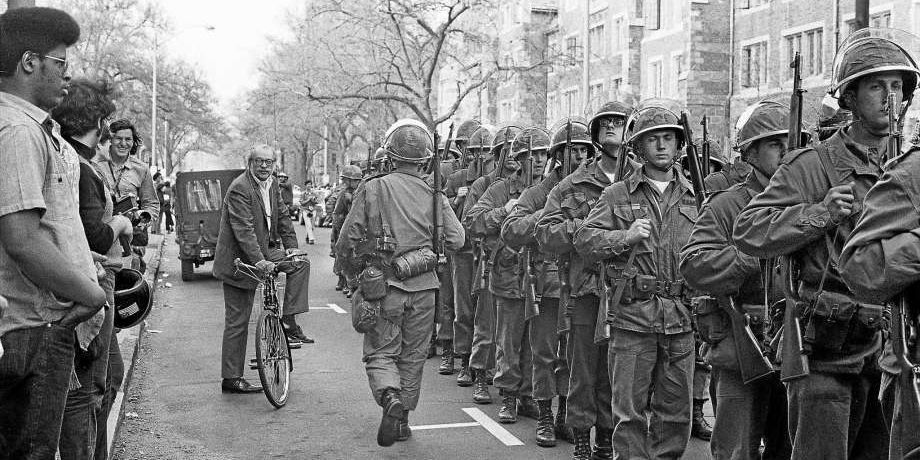 Chester Kerr, head of the Yale University Press, bicycles between lines of protesters and National Guard.  Tom Strong.